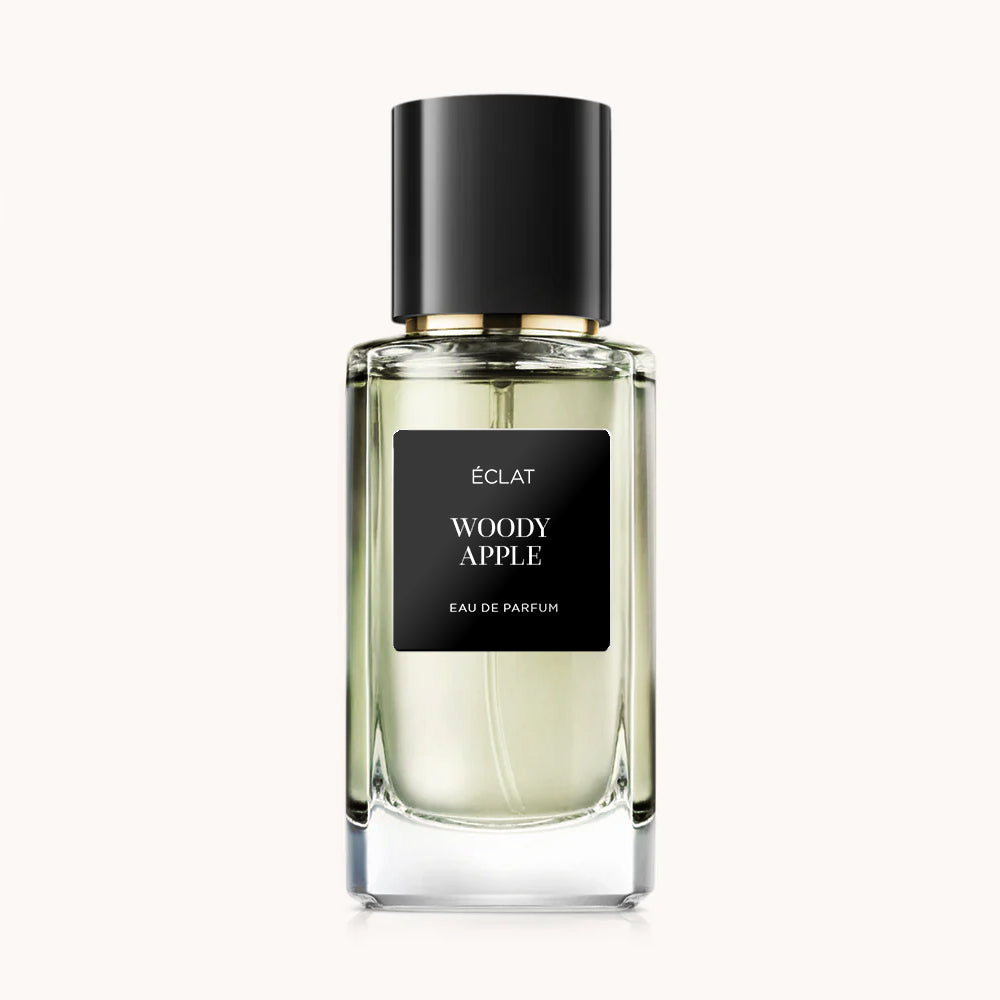 Flacon of the men's perfume dupe ÉCLAT Woody Apple, an elegant transparent glass bottle with a black cylindrical magnetic cap and a black label. The label displays the brand name ÉCLAT, the name Woody Apple, and the phrase “Eau de Parfum”.