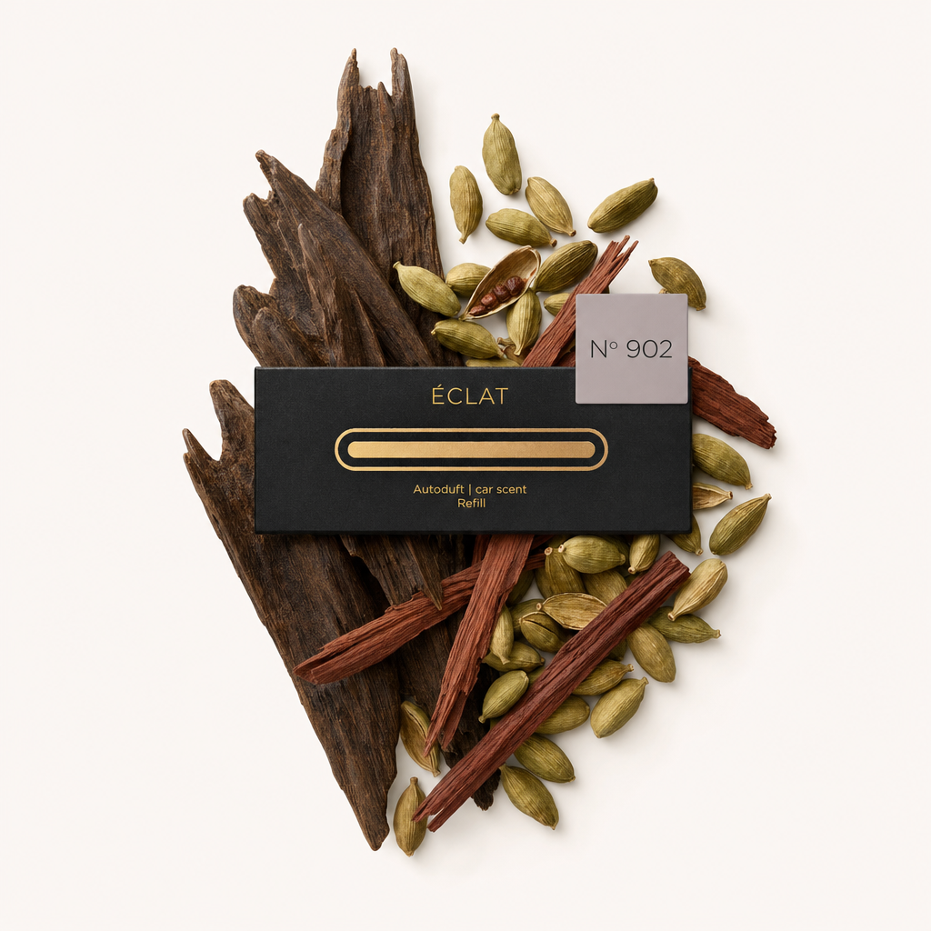 Un arrangiamento di baccelli di cardamomo e legni aromatici circonda un tappo nero ÉCLAT con un'etichetta che riporta il numero 902.