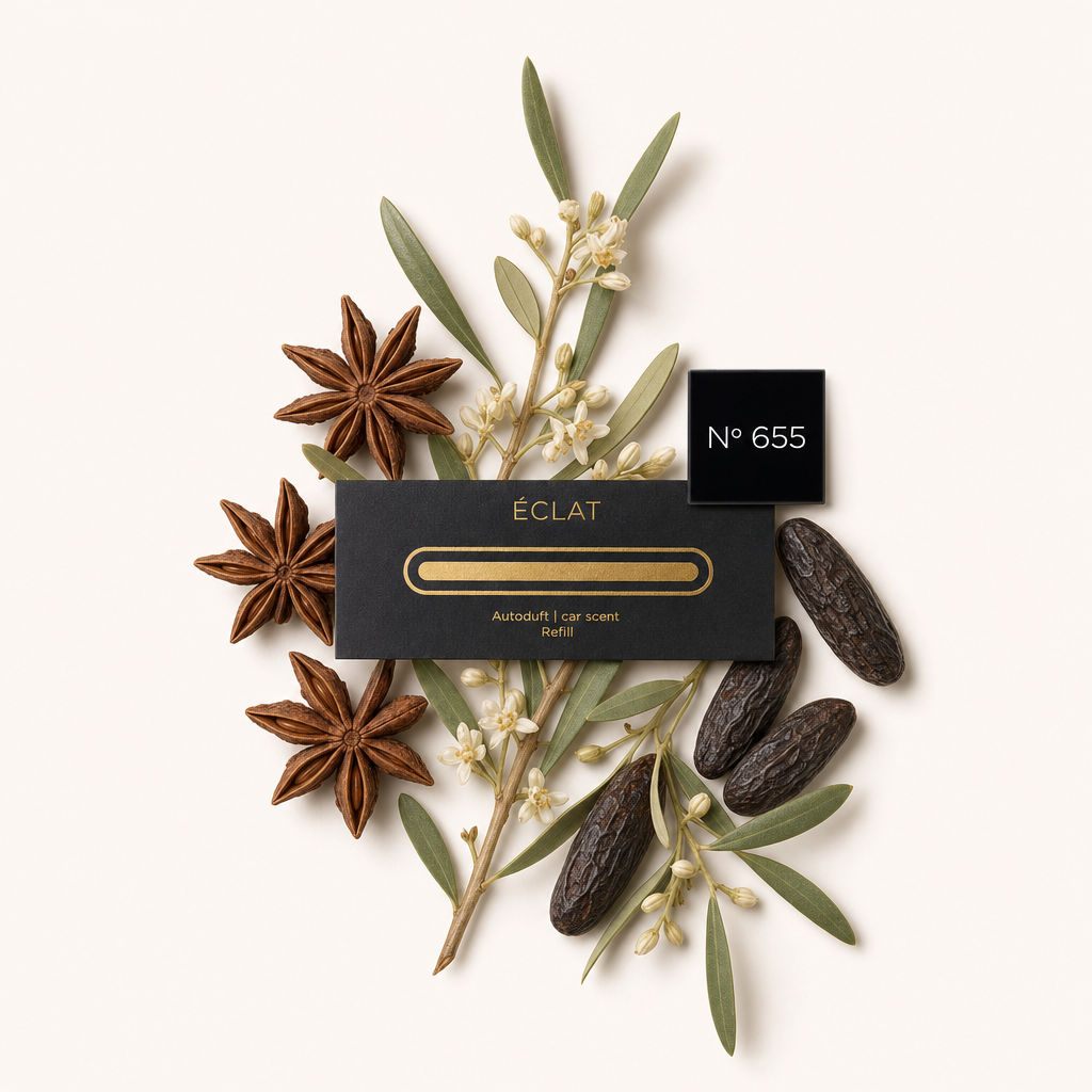 Un arrangiamento di anice stellato, fiori bianchi, olive e fagioli tonka circonda un tappo nero ÉCLAT con etichetta dorata per ricarica profumo auto n° 655.