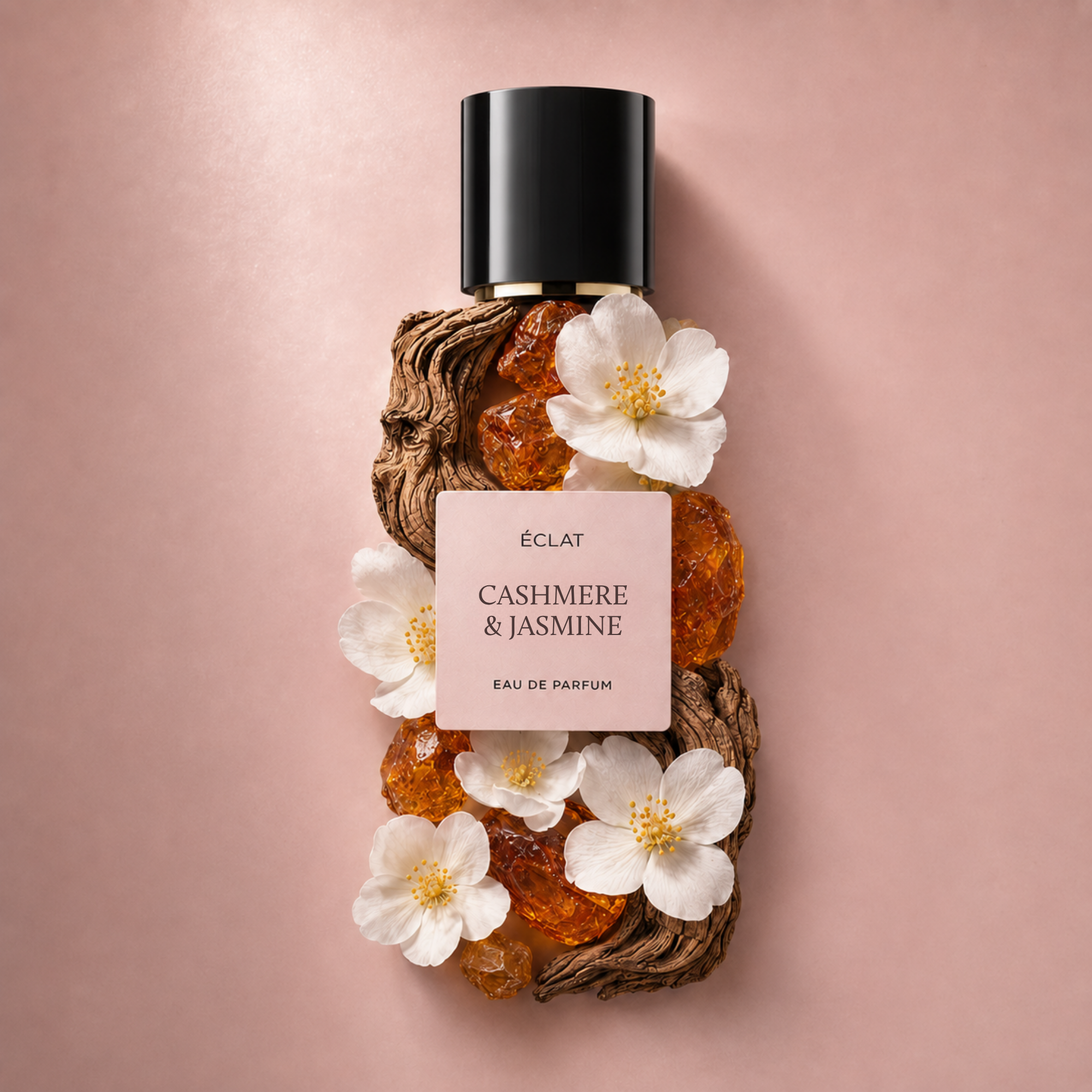 Flacone di profumo ÉCLAT Cashmere & Jasmine decorato con fiori bianchi e cristalli d'ambra su sfondo rosa.
