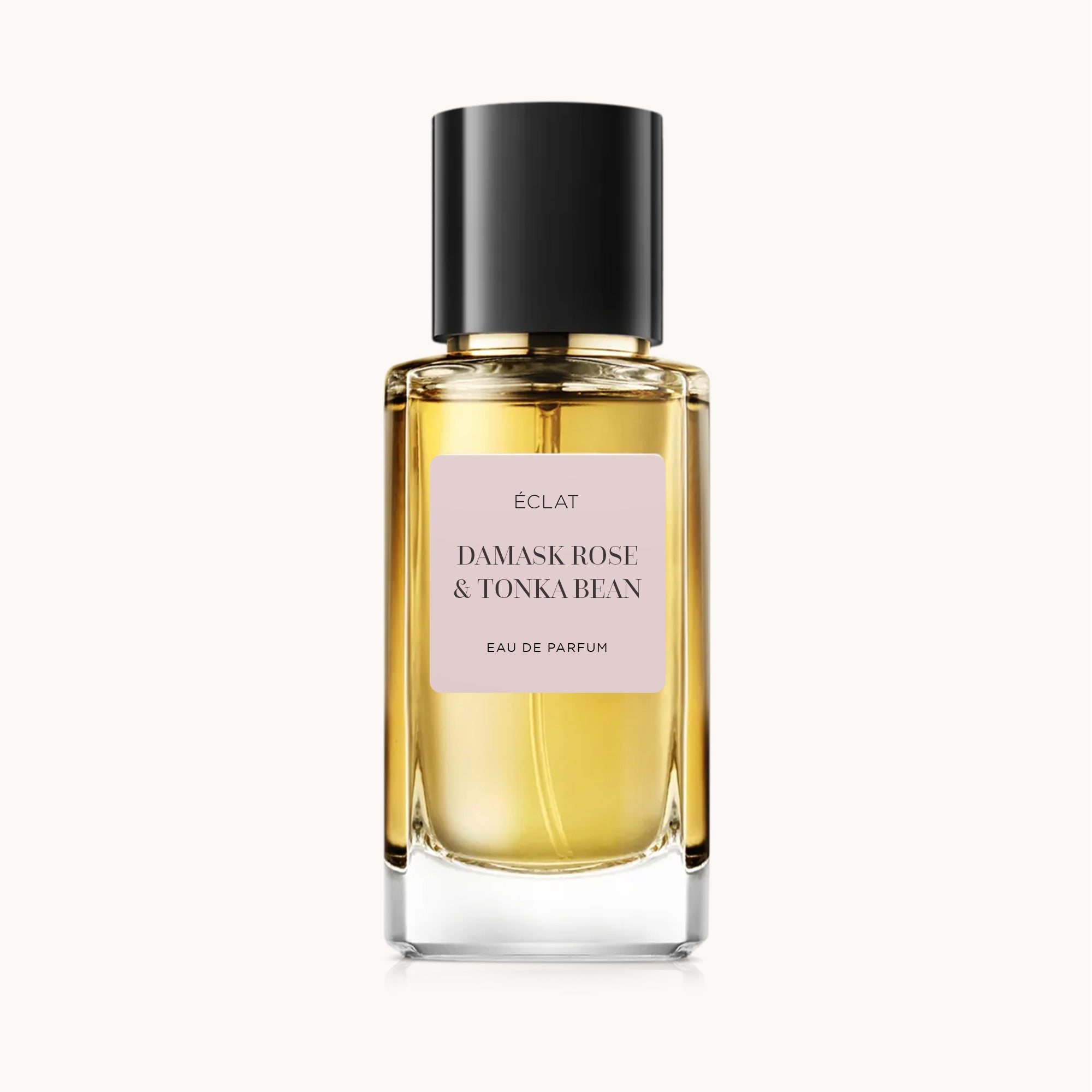 Bottiglia di vetro sfaccettato con tonalità dorata e tappo nero opaco, con etichetta rosa di ÉCLAT Damask Rose & Tonka Bean.