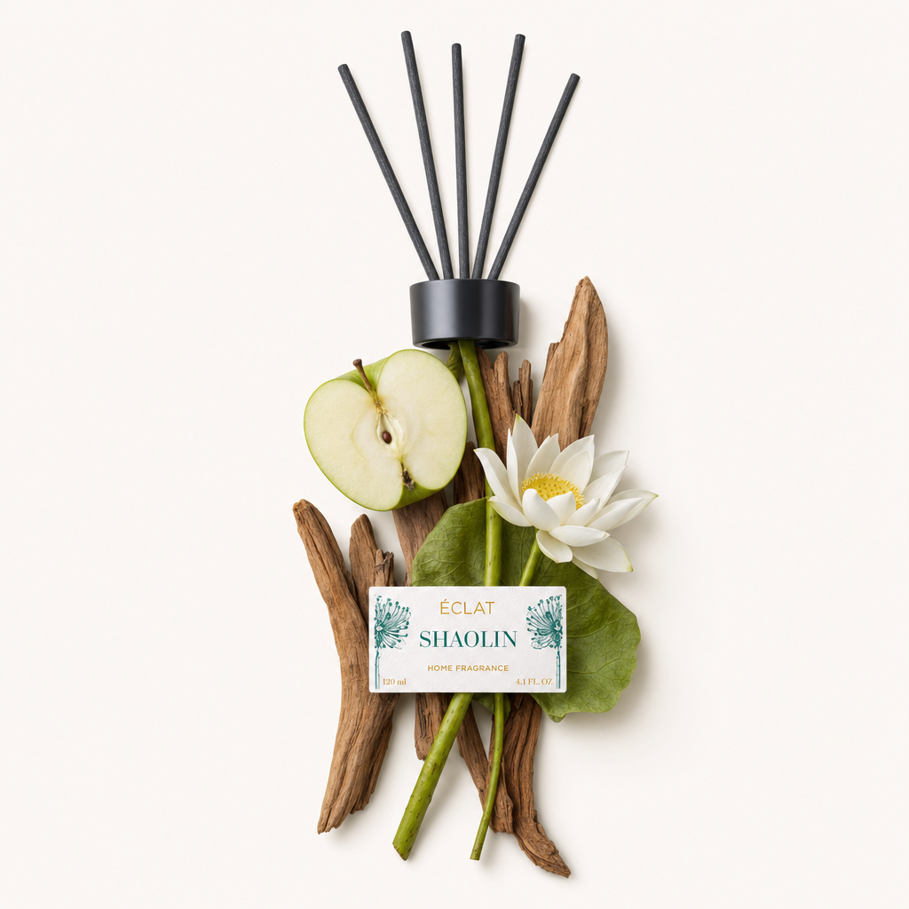 Un insieme di bastoncini di legno, una mela verde tagliata a metà, un fiore di loto bianco e foglie è elegantemente disposto attorno al tappo nero con etichetta degli ÉCLAT Shaolin Room Fragrance Sticks.