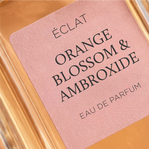Un flacone in vetro sfaccettato con un'etichetta rosa che mostra il nome ÉCLAT Orange Blossom & Ambroxide.