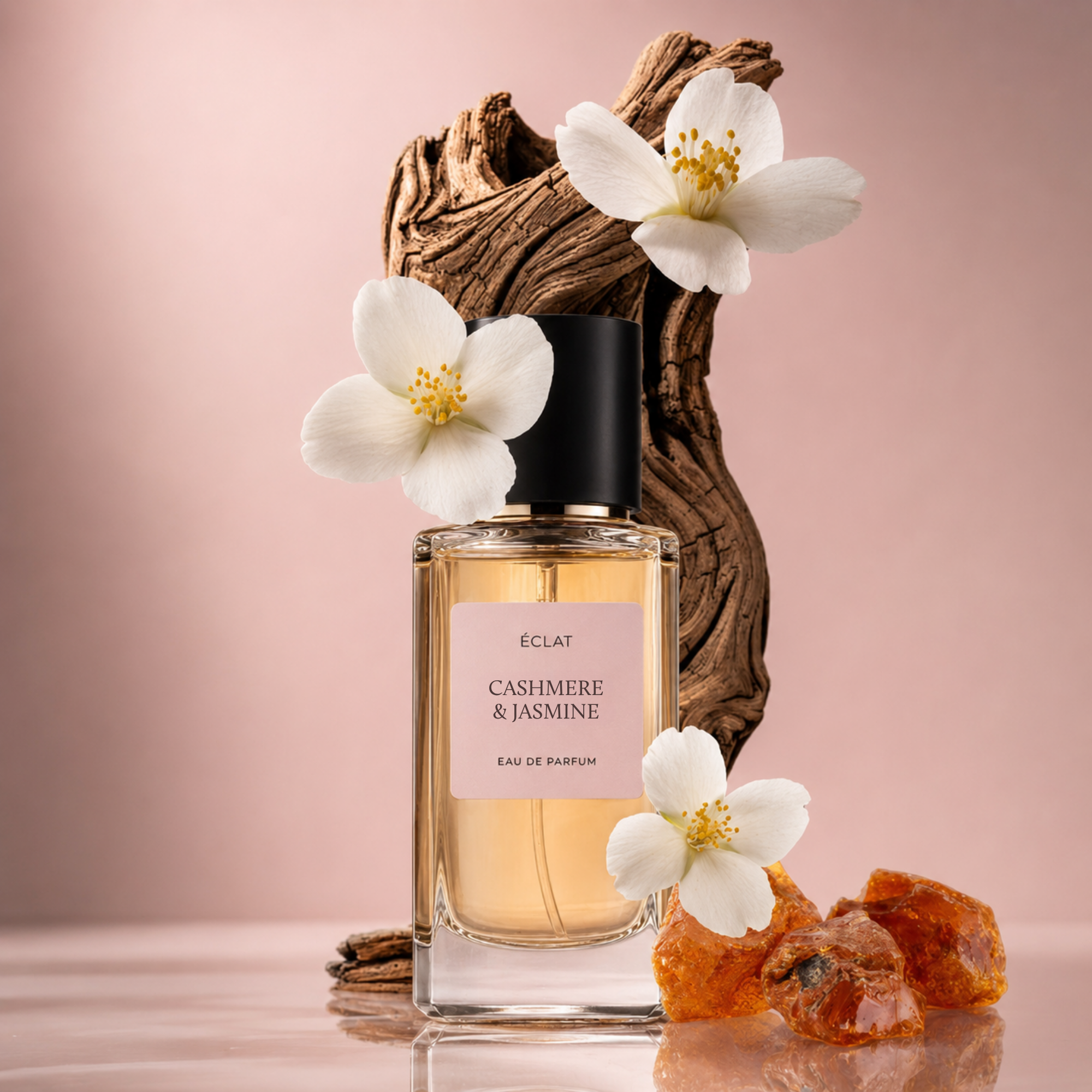 Una bottiglia di vetro trasparente di profumo ÉCLAT Cashmere & Jasmine con tappo nero, circondata da fiori di gelsomino bianchi e pietre d'ambra su uno sfondo di legno texturizzato.