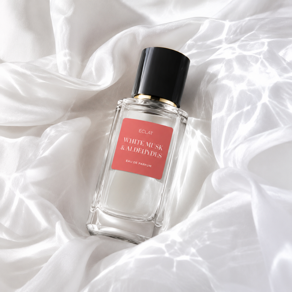 Un flacone in vetro sfaccettato di ÉCLAT White Musk & Aldehydes con tappo nero ed etichetta corallo su sfondo di tessuto satinato.