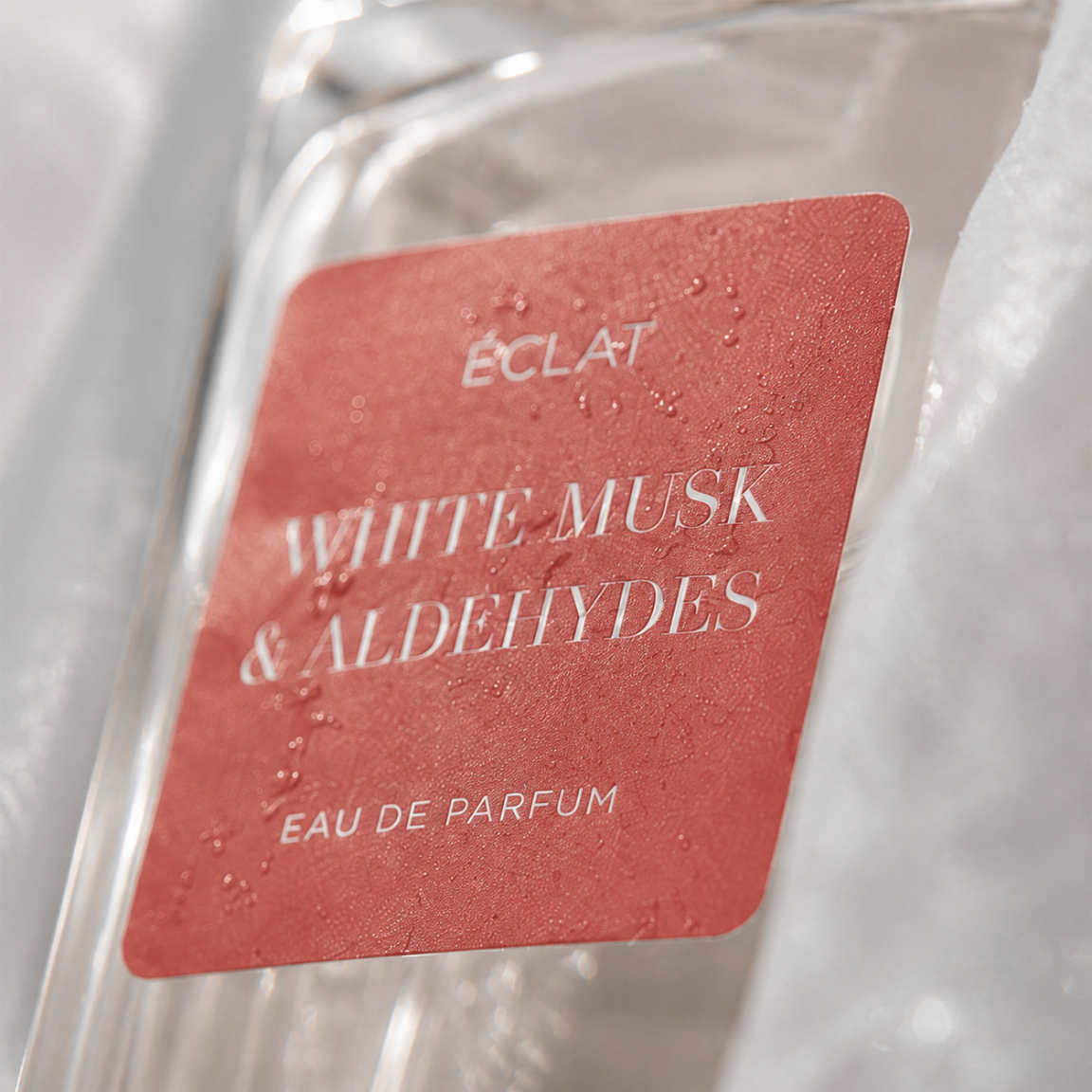 Primo piano del flacone di profumo ÉCLAT White Musk & Aldehydes con etichetta rossa testurizzata.