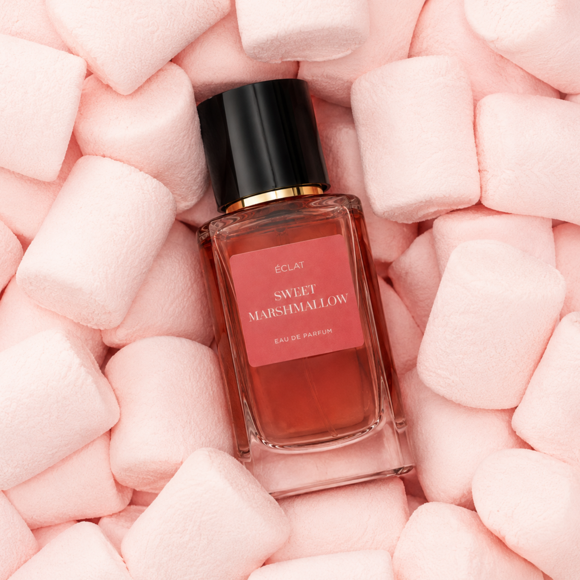 Una bottiglia di vetro di ÉCLAT Sweet Marshmallow circondata da soffici marshmallow rosa, con tappo nero ed etichetta rosa.