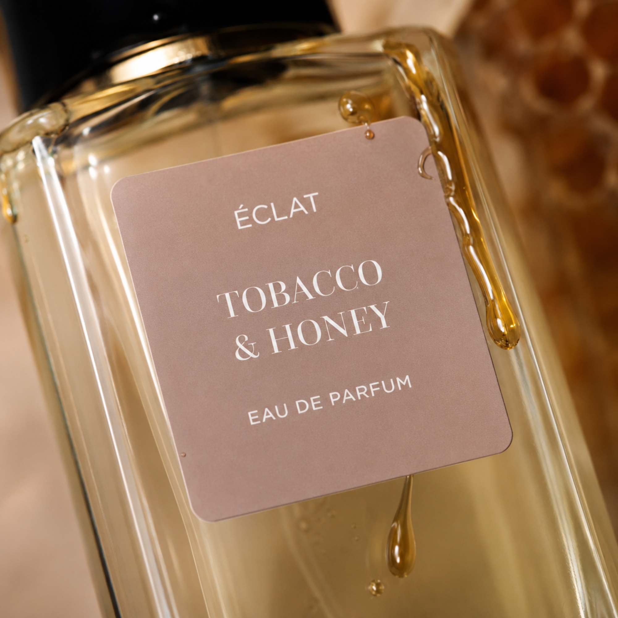 Flacone di profumo ÉCLAT Tobacco & Honey con etichetta opaca marrone chiaro e una goccia di miele che scorre sulla superficie di vetro.