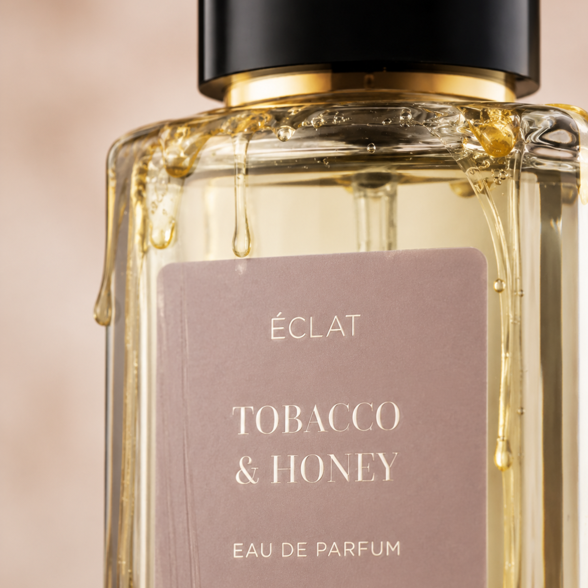 Un flacone in vetro sfaccettato di ÉCLAT Tobacco & Honey con etichetta satinata e tappo nero, decorato con gocce di miele.