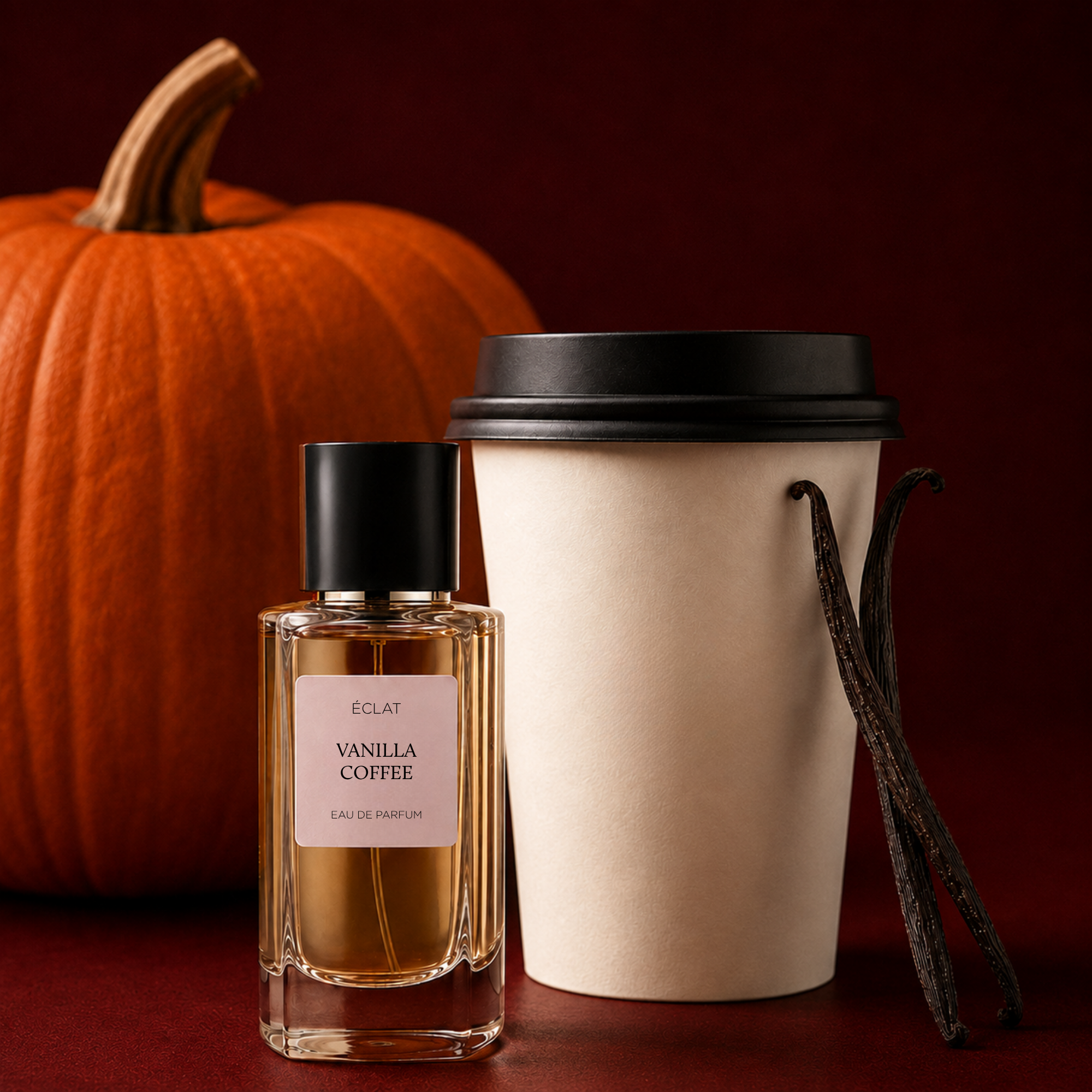 Un flacone in vetro sfaccettato di ÉCLAT Vanilla Coffee con tappo nero è posizionato accanto a una tazza da caffè da asporto e baccelli di vaniglia, con una zucca sullo sfondo.
