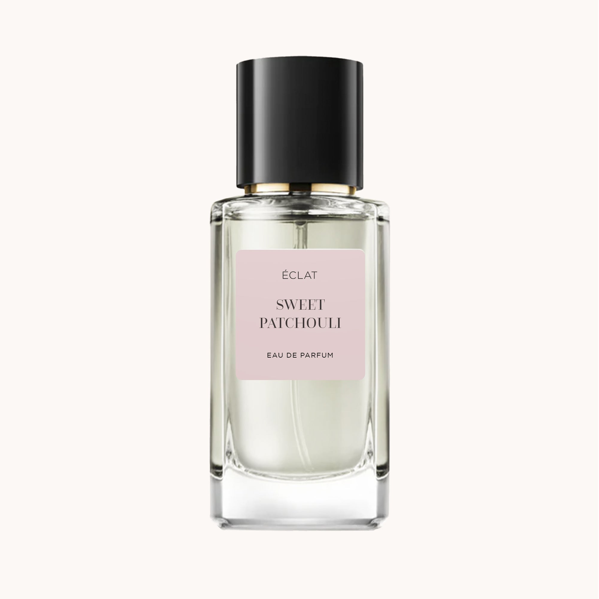 Un flacone in vetro sfaccettato di ÉCLAT Sweet Patchouli con tappo nero e etichetta rosa tenue.