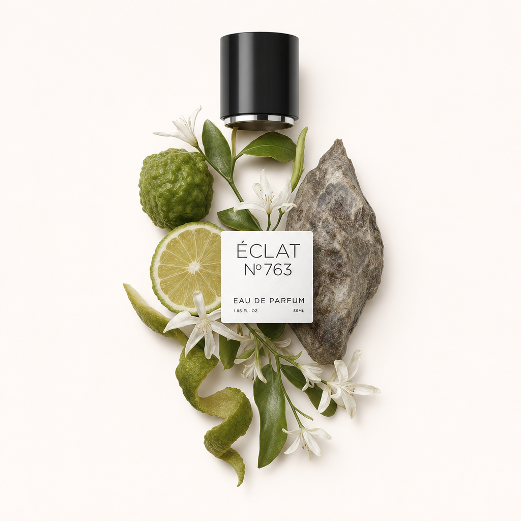 Una composizione di bergamotto, fette di lime, foglie verdi e piccoli fiori bianchi circonda un tappo nero con etichetta ÉCLAT Ambergris & Bergamot.