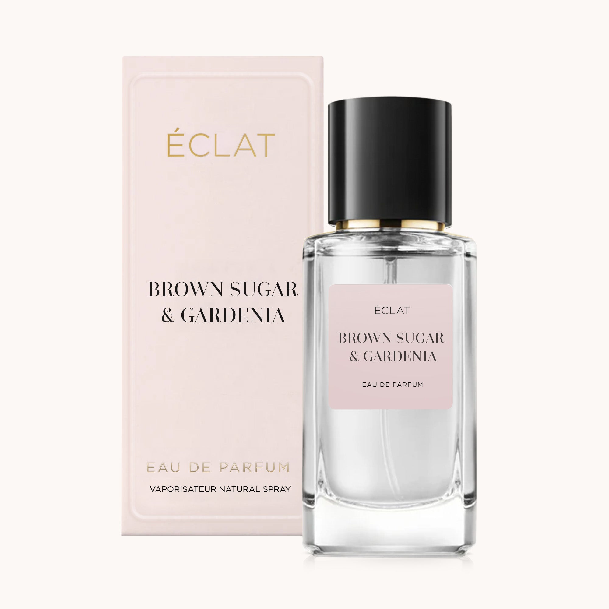 Un flacone in vetro sfaccettato del profumo ÉCLAT Brown Sugar & Gardenia con tappo nero, accanto a una scatola di presentazione rosa tenue.