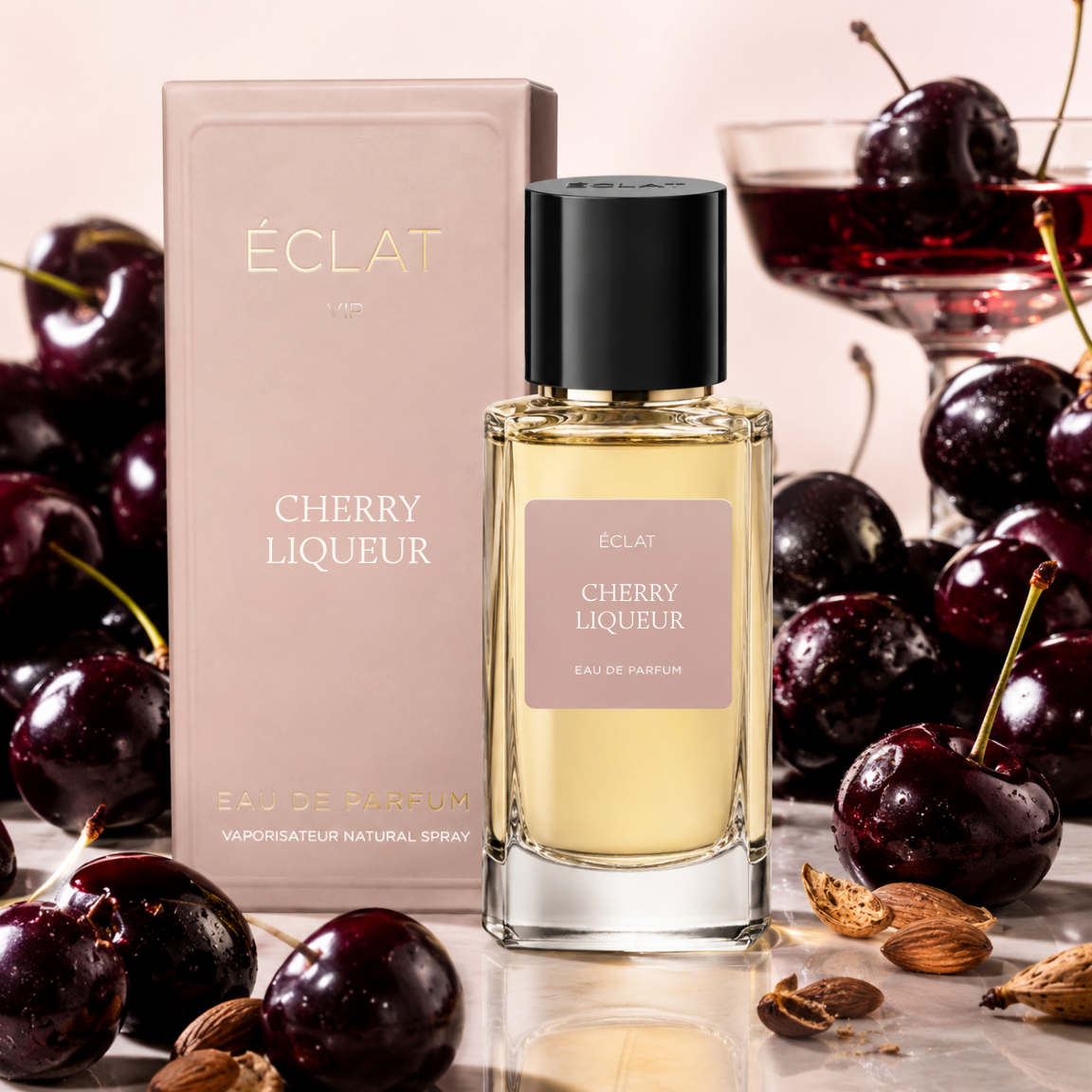 L'immagine mostra il profumo ÉCLAT Cherry Liqueur con un flacone in vetro sfaccettato e tappo nero, accanto a una scatola rosa e ciliegie fresche.
