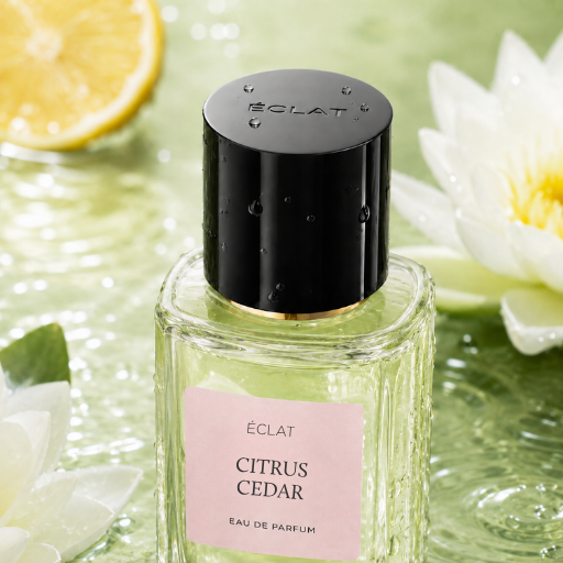 Flacone in vetro sfaccettato di ÉCLAT Citrus Cedar con tappo nero su una superficie d'acqua con fetta di limone e fiori bianchi.