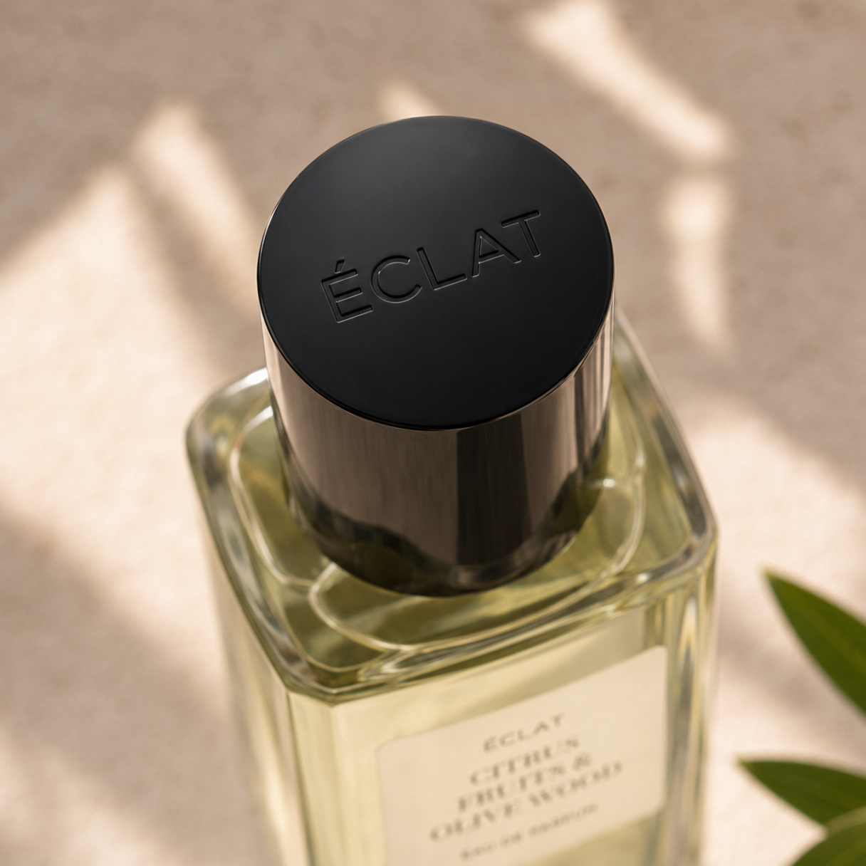 Boccetta di vetro sfaccettato di ÉCLAT Citrus Fruits & Olive Wood con elegante tappo nero su sfondo morbido.