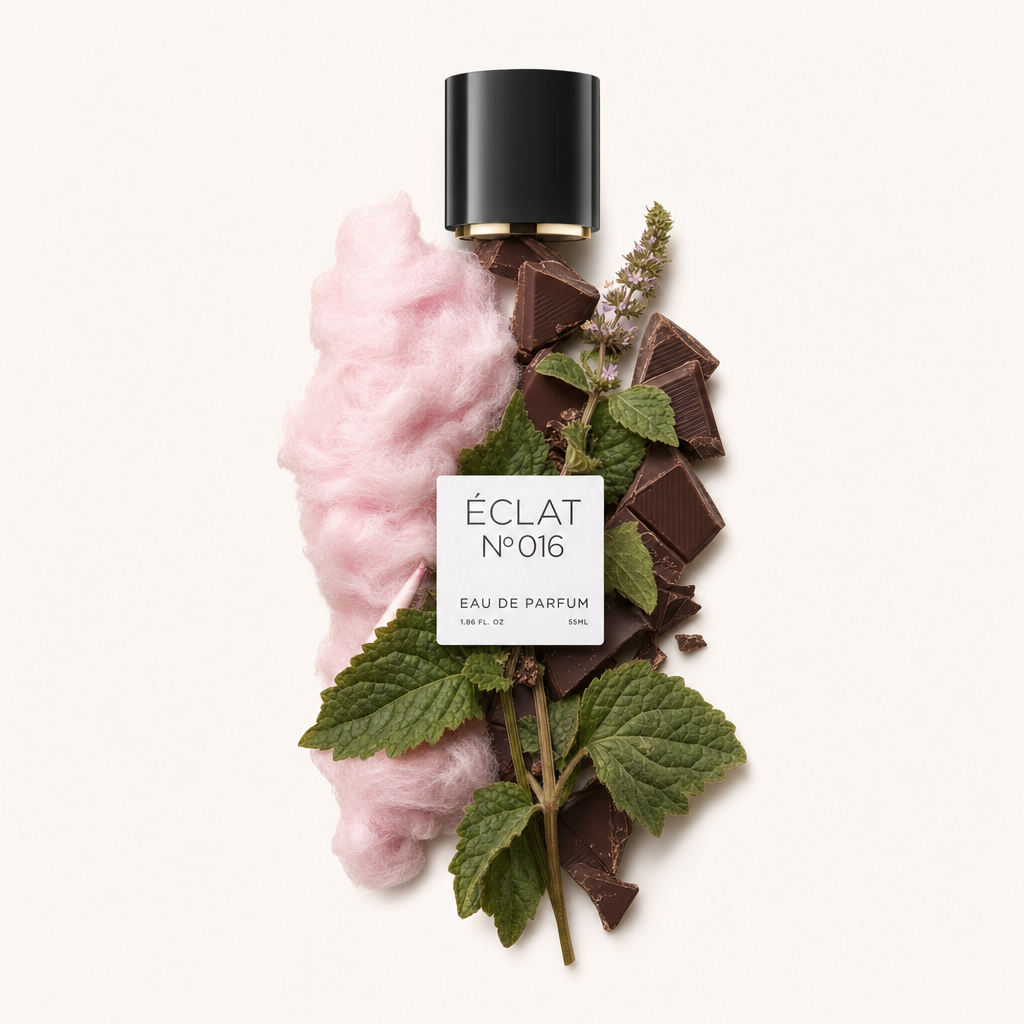 Un arrangiamento di zucchero filato rosa, pezzi di cioccolato e foglie verdi di patchouli circonda un tappo nero con etichetta, rappresentando ÉCLAT Cotton Candy & Patchouli.