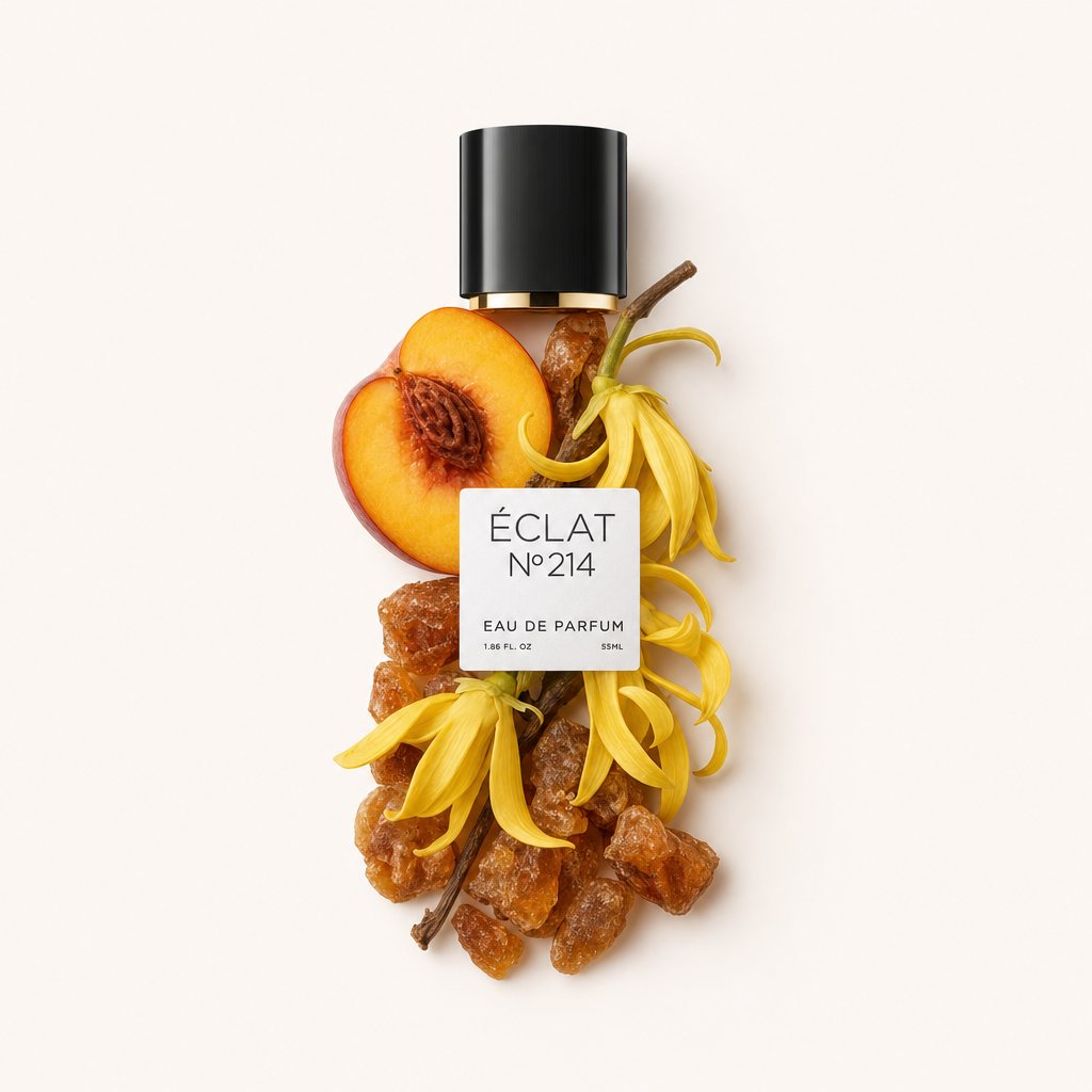 Un arrangiamento di fiori di ylang-ylang gialli, resina d'ambra e una pesca tagliata a metà circondano un tappo nero con etichetta per ÉCLAT Creamy Amber.