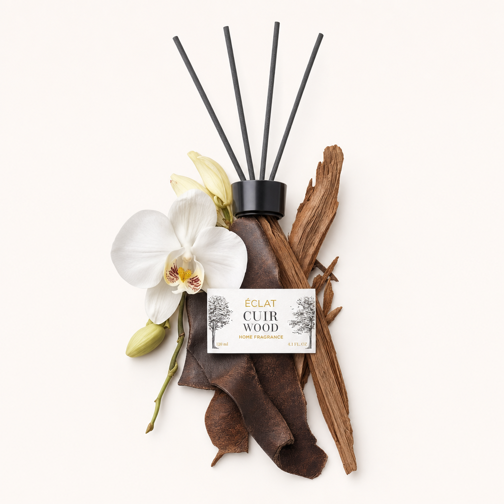 Ingredienti artisticamente disposti di ÉCLAT Cuir Wood, con orchidea, pelle e pezzi di legno accanto al tappo nero con etichetta.