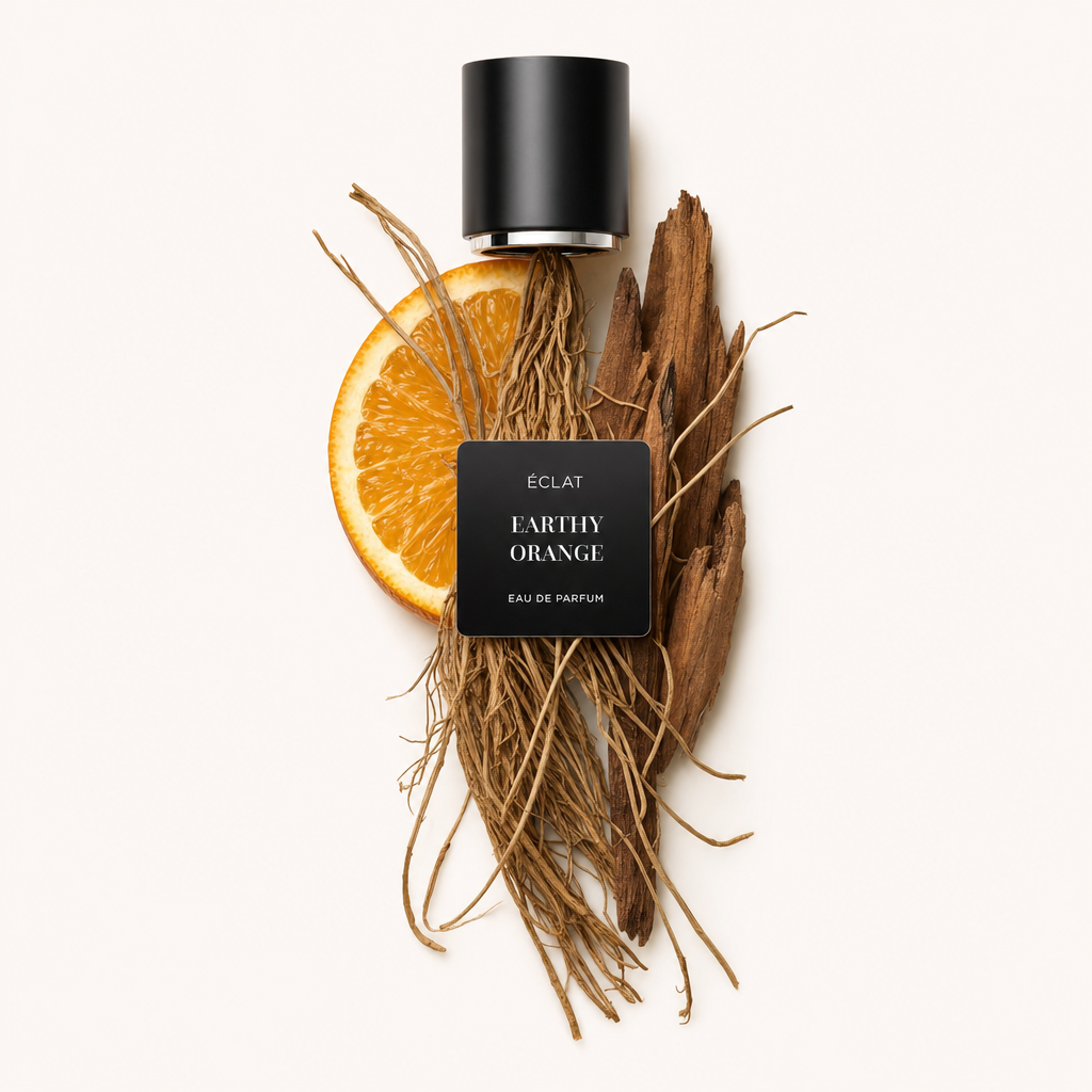 Una composizione di radici terrose, una fetta d'arancia e pezzi di legno sotto un tappo nero con etichetta ÉCLAT Earthy Orange.