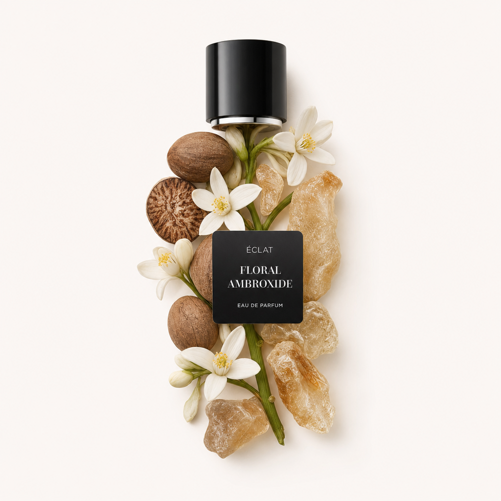 Un arrangiamento di fiori bianchi, noci essiccate e resina ambrata, con un tappo nero etichettato ÉCLAT Floral Ambroxide sopra.