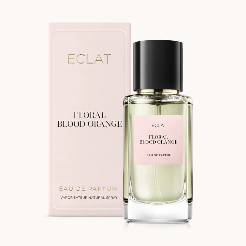 Un flacone in vetro sfaccettato di ÉCLAT Floral Blood Orange con tappo nero accanto a una scatola rosa pallido.
