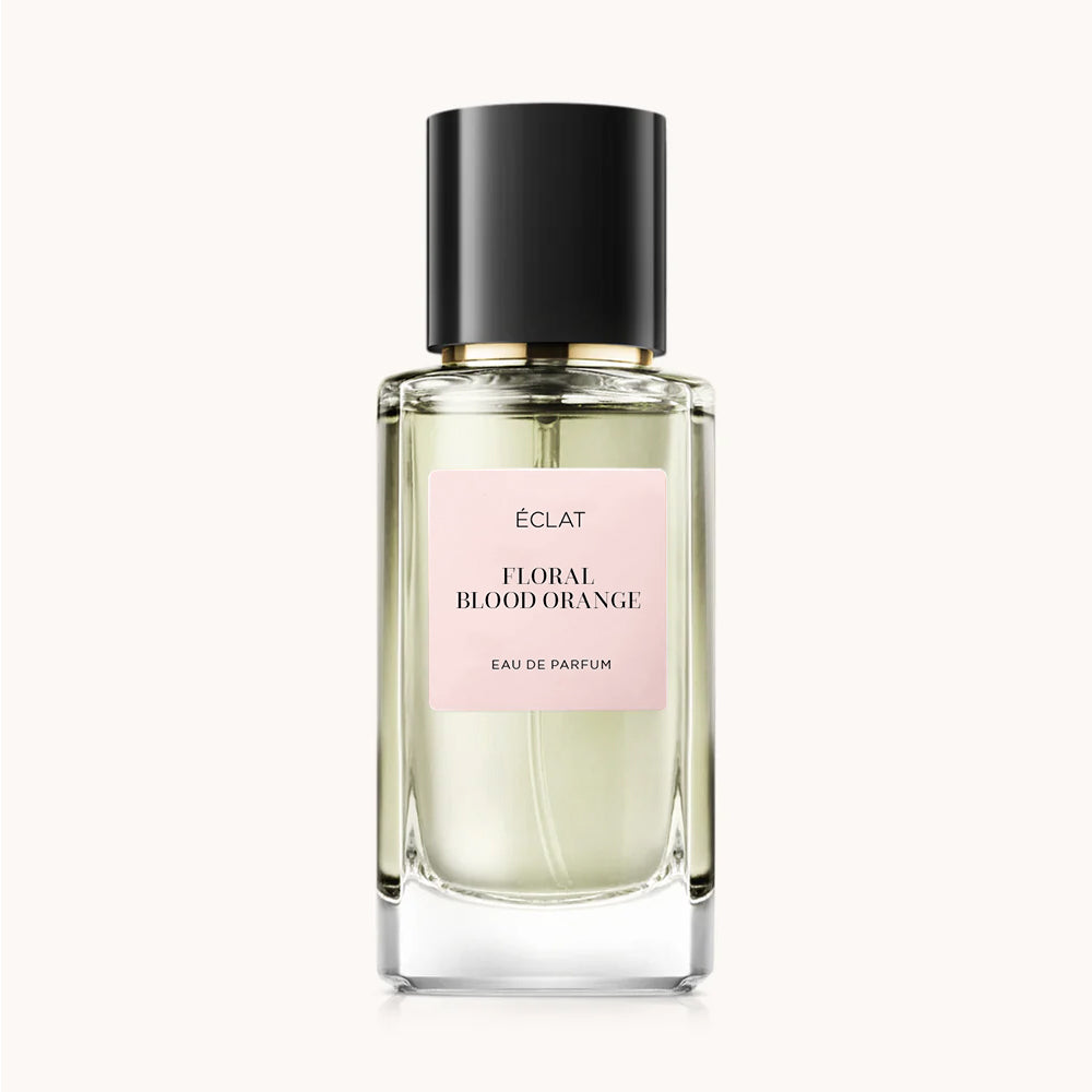 Un flacone di vetro sfaccettato con tappo nero ed etichetta rosa per il profumo ÉCLAT Floral Blood Orange.