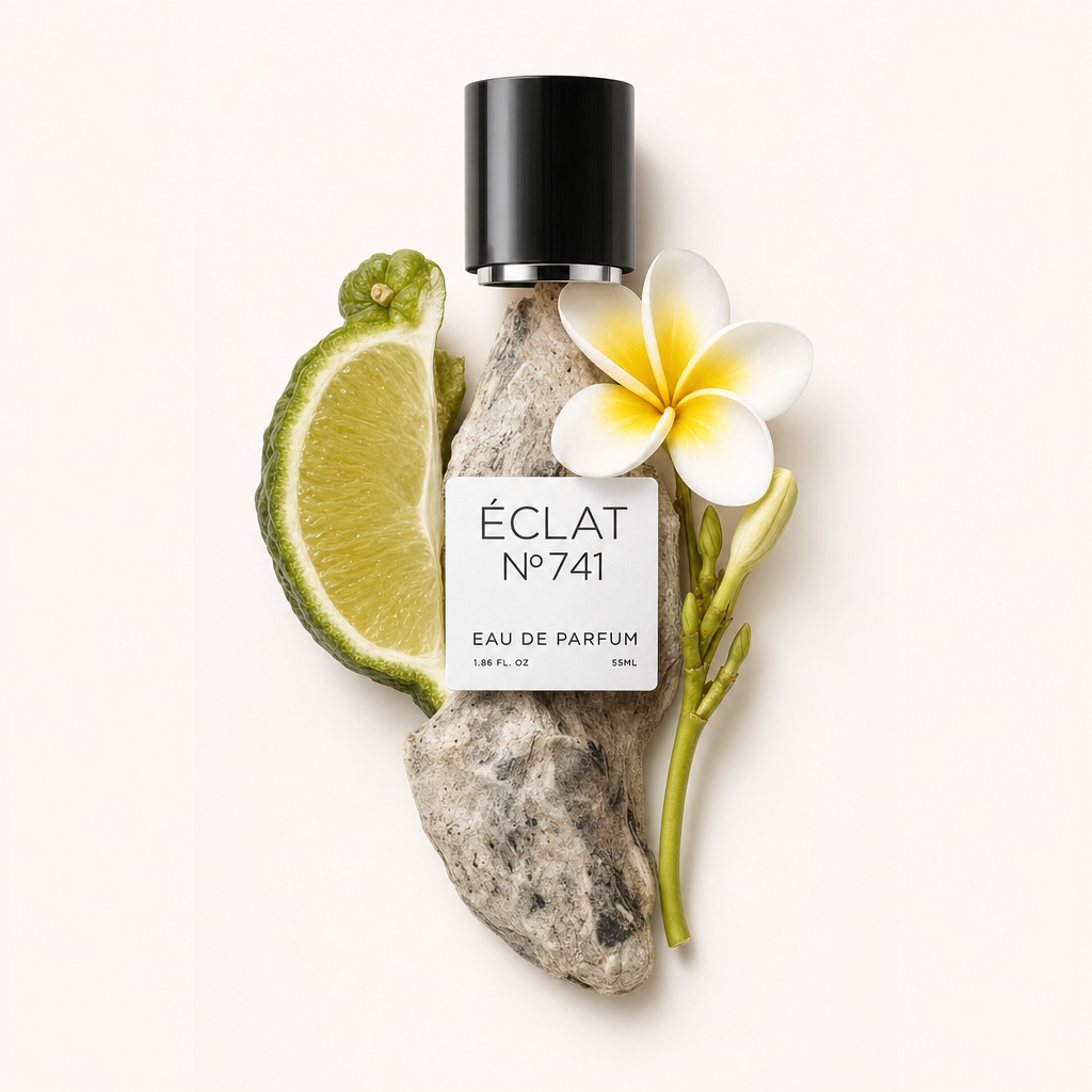 Un tappo nero con etichetta è circondato da cardamomo fresco, una fetta di lime e un plumeria bianco su un pezzo di legno fluitato chiaro.
