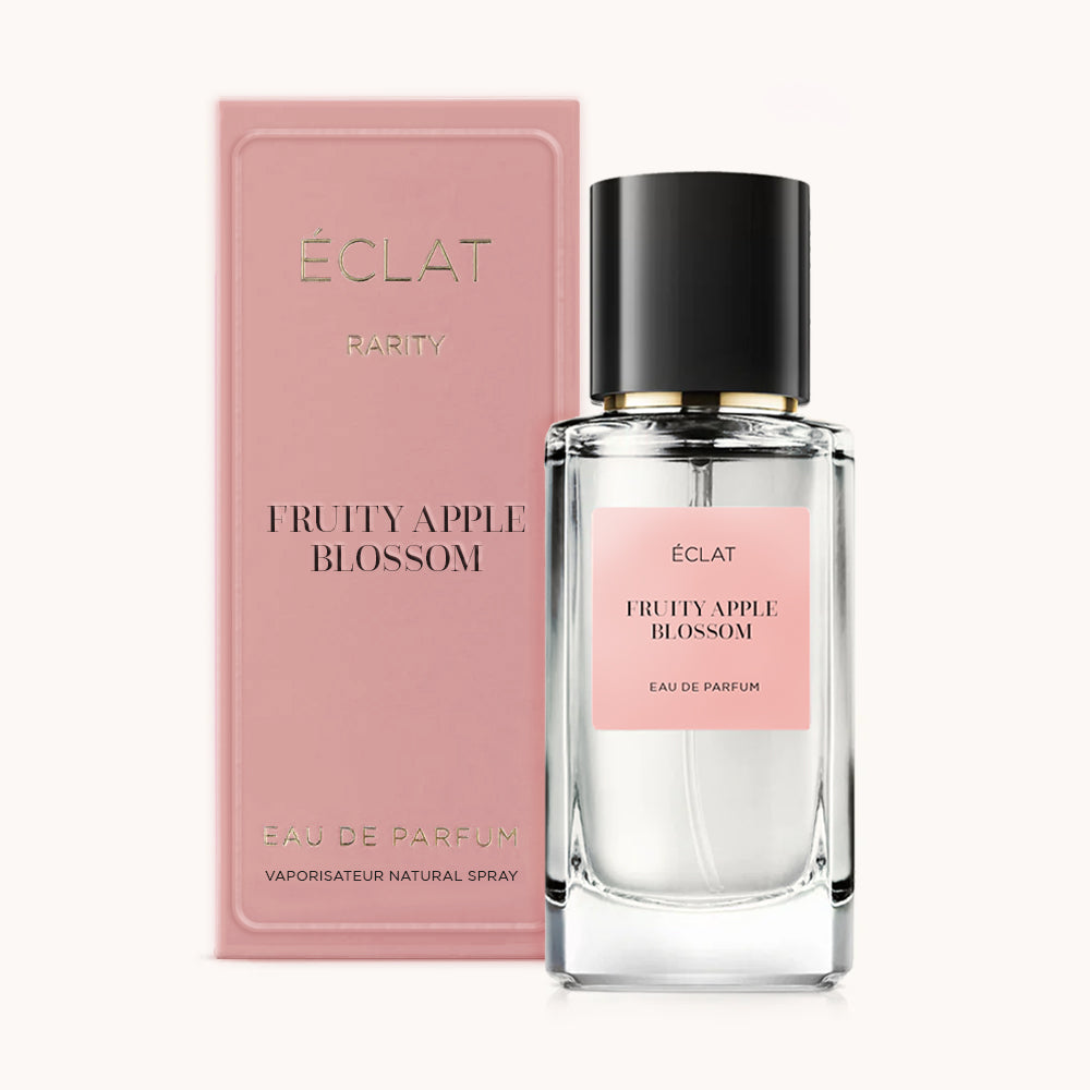 Una bottiglia di vetro sfaccettato con etichetta rosa e tappo nero, accanto a una scatola rosa coordinata, presenta ÉCLAT Fruity Apple Blossom.