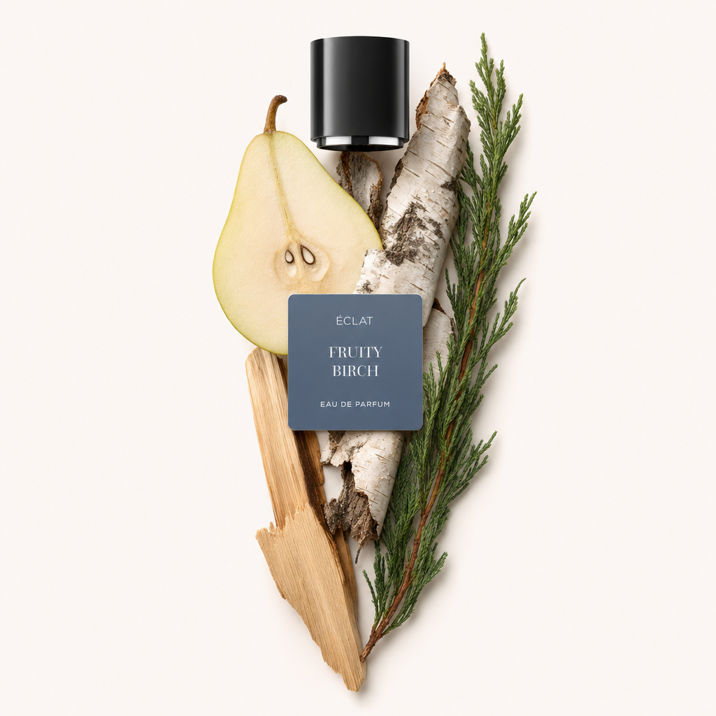 Un arrangiamento artistico con una pera tagliata, corteccia di betulla e rami di cipresso, sormontato da un tappo nero etichettato ÉCLAT Fruity Birch.