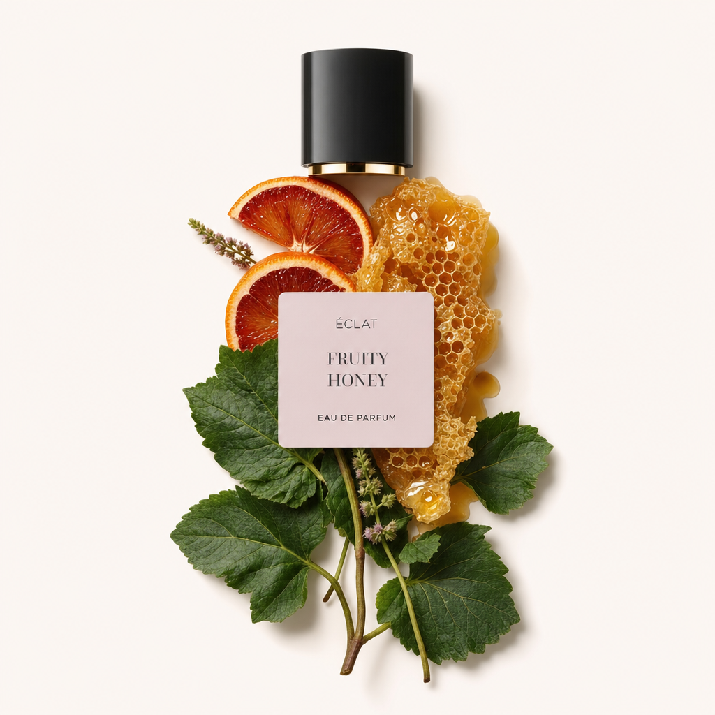 Una composizione di fette di arancia rossa matura, foglie verdi rigogliose e nido d'ape disposte intorno al tappo nero con l'etichetta del profumo ÉCLAT Fruity Honey.
