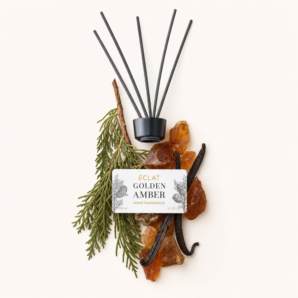 Una natura morta accuratamente disposta con rami di cedro, pietre d'ambra e baccelli di vaniglia attorno a un tappo nero con etichetta ÉCLAT Golden Amber.