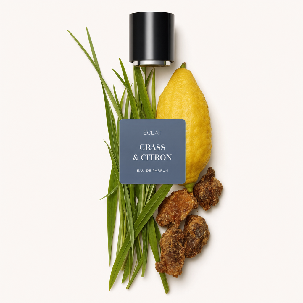Una composizione di fili d'erba, un cedro intero e pezzi di resina è presentata con un tappo nero con etichetta di ÉCLAT Grass & Citron.
