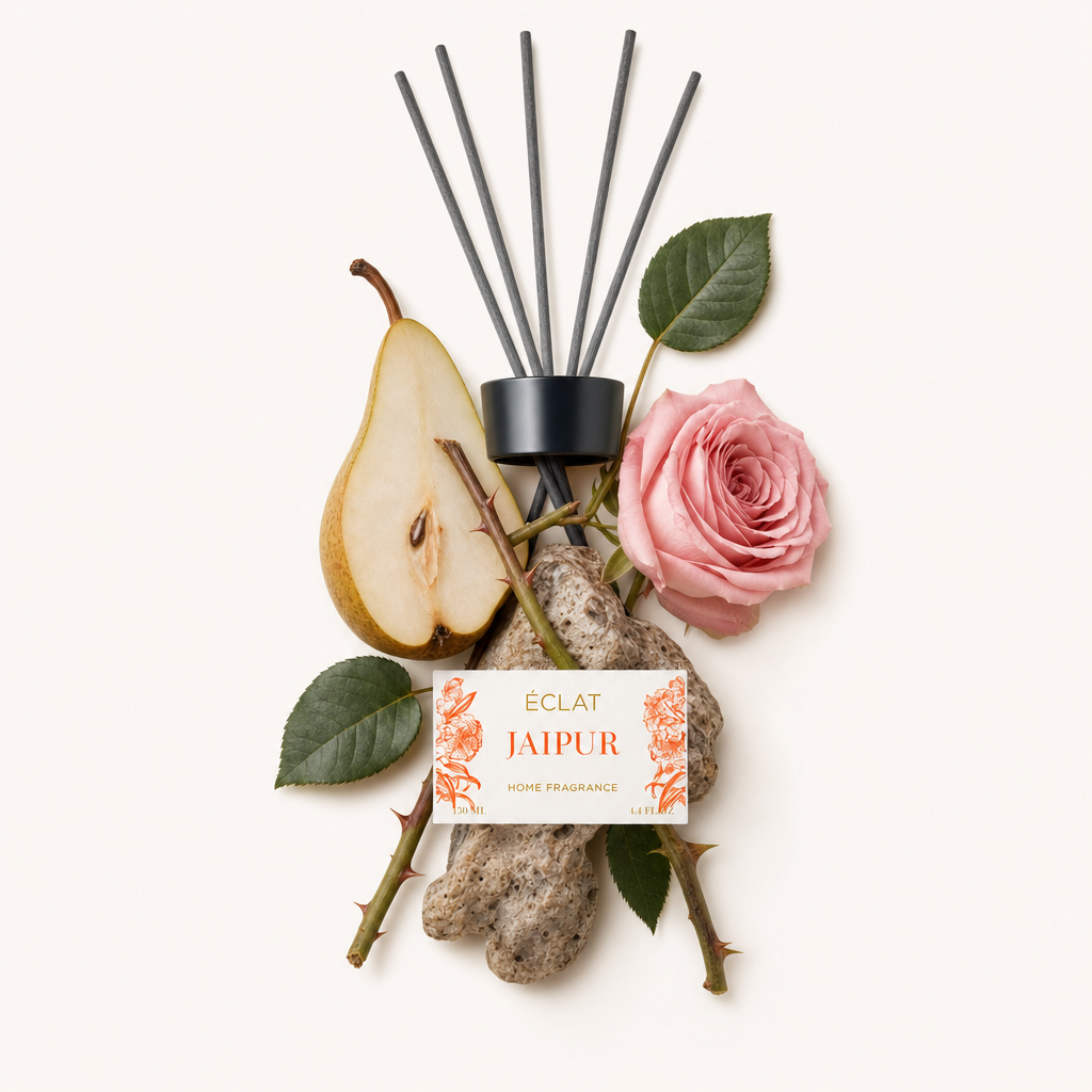 Una disposizione di note di fragranza ÉCLAT Jaipur con una rosa, fetta di pera, foglie verdi e pietre strutturate, accanto a un tappo nero con etichetta.