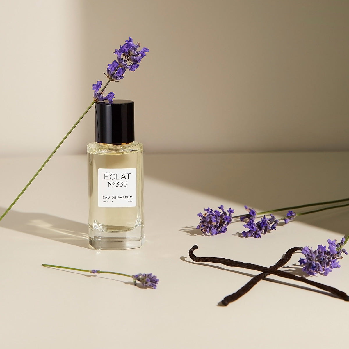 Flacone di vetro sfaccettato di ÉCLAT Lavender & Vanilla con tappo nero, circondato da rametti di lavanda e baccelli di vaniglia.