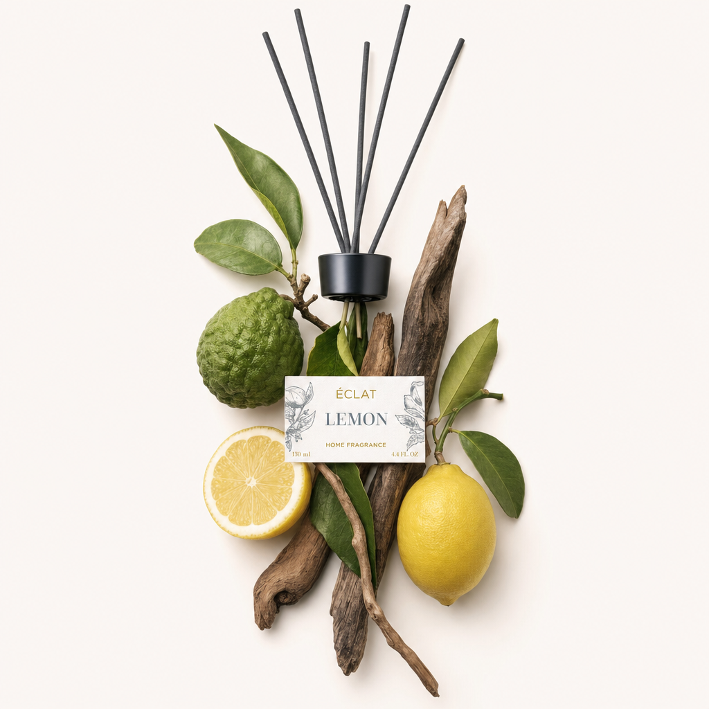 Una composizione di ingredienti con limone, bergamotto e pezzi di legno che circondano un tappo nero con bastoncini e un'etichetta per ÉCLAT Lemon Room Fragrance Sticks.