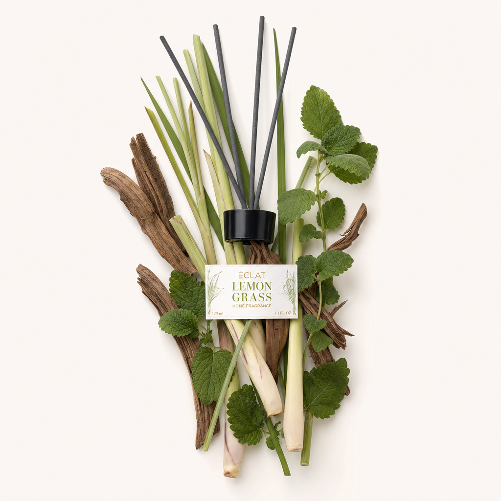Un arrangiamento di citronella, foglie di menta e pezzi di legno circonda il tappo nero con l'etichetta ÉCLAT Lemongrass Room Fragrance Sticks.