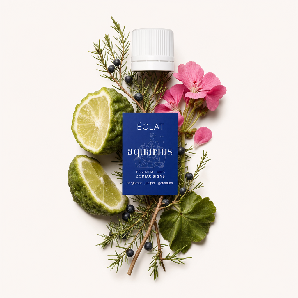 Un arrangiamento di fette di bergamotto, rami di ginepro con bacche e fiori di geranio rosa circonda un tappo nero con etichetta dell'olio essenziale Aquarius di ÉCLAT.