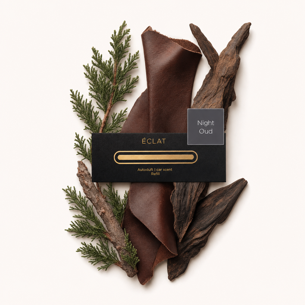 Una disposizione di rami di cedro, striscia di cuoio e legno oud con un tappo nero ÉCLAT etichettato 'Night Oud'.