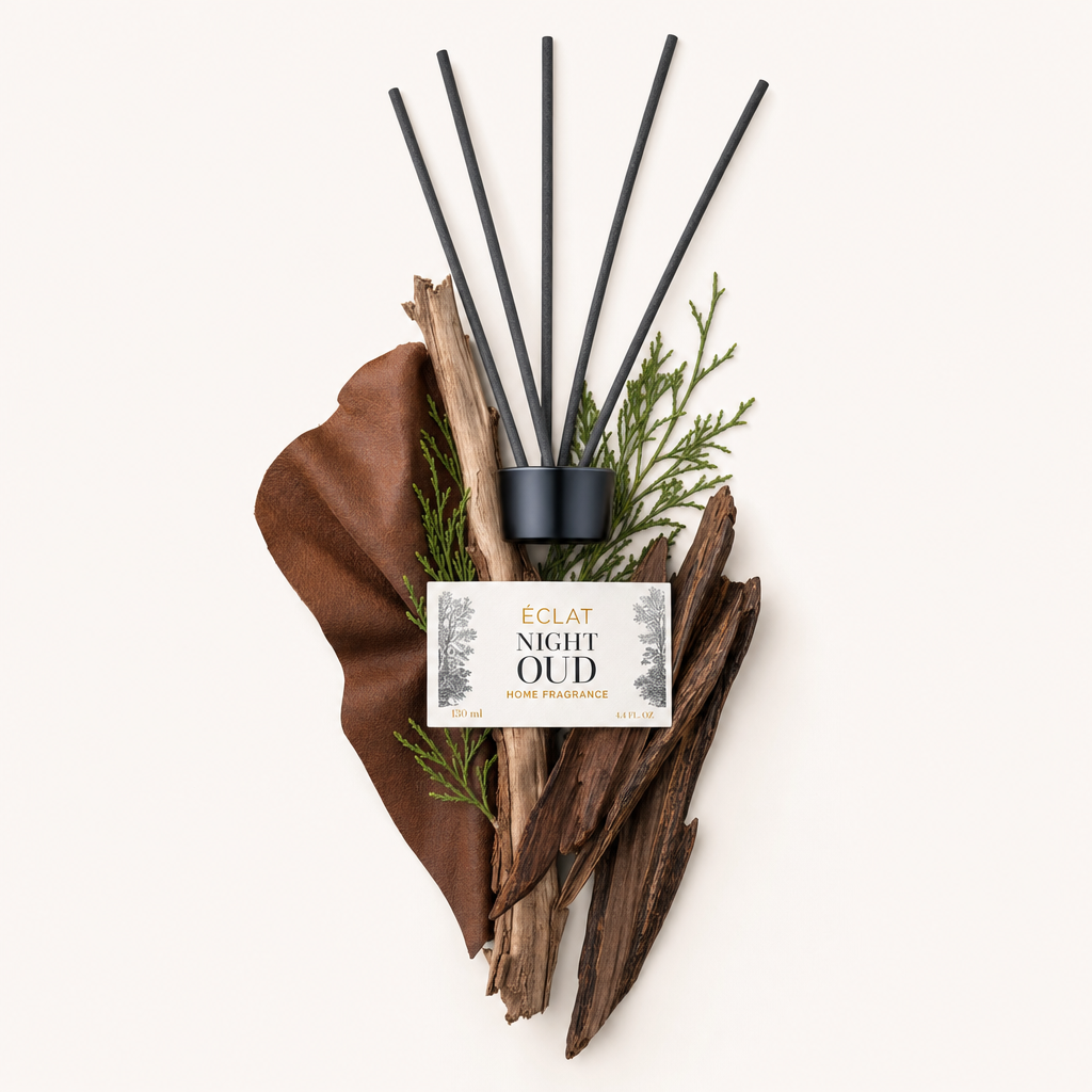 Un arrangiamento di ingredienti della fragranza ÉCLAT Night Oud tra cui legno secco, rametti verdi e un elemento cuoio, sormontato da un tappo nero con etichetta.