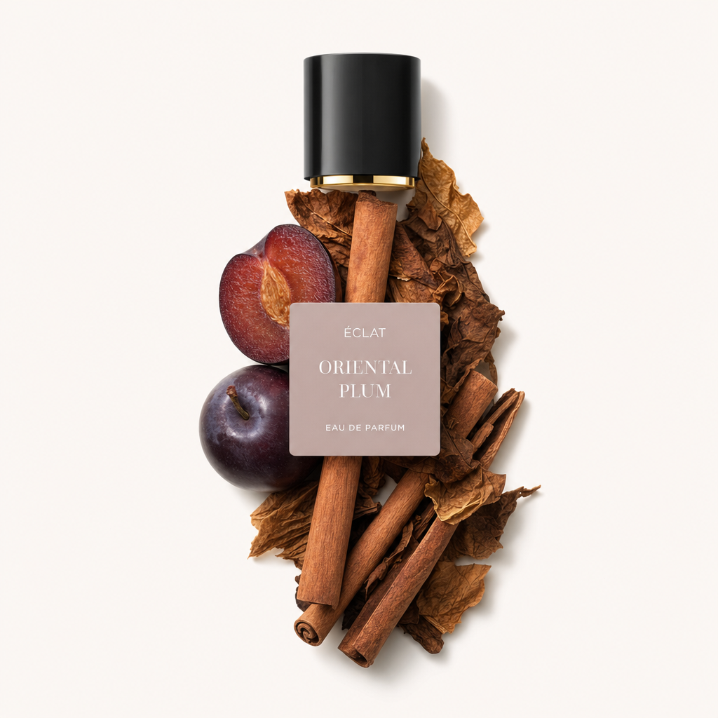 Un arrangiamento di bastoncini di cannella, foglie di tabacco essiccate e prugne mature circonda un tappo nero con accenti dorati con etichetta ÉCLAT Oriental Plum.