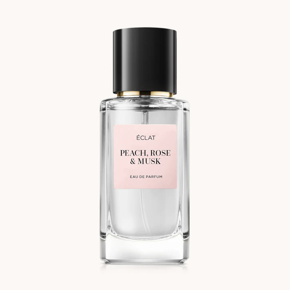 Bottiglia in vetro sfaccettato di ÉCLAT Peach, Rose & Musk con etichetta rosa opaca e tappo nero lucido.