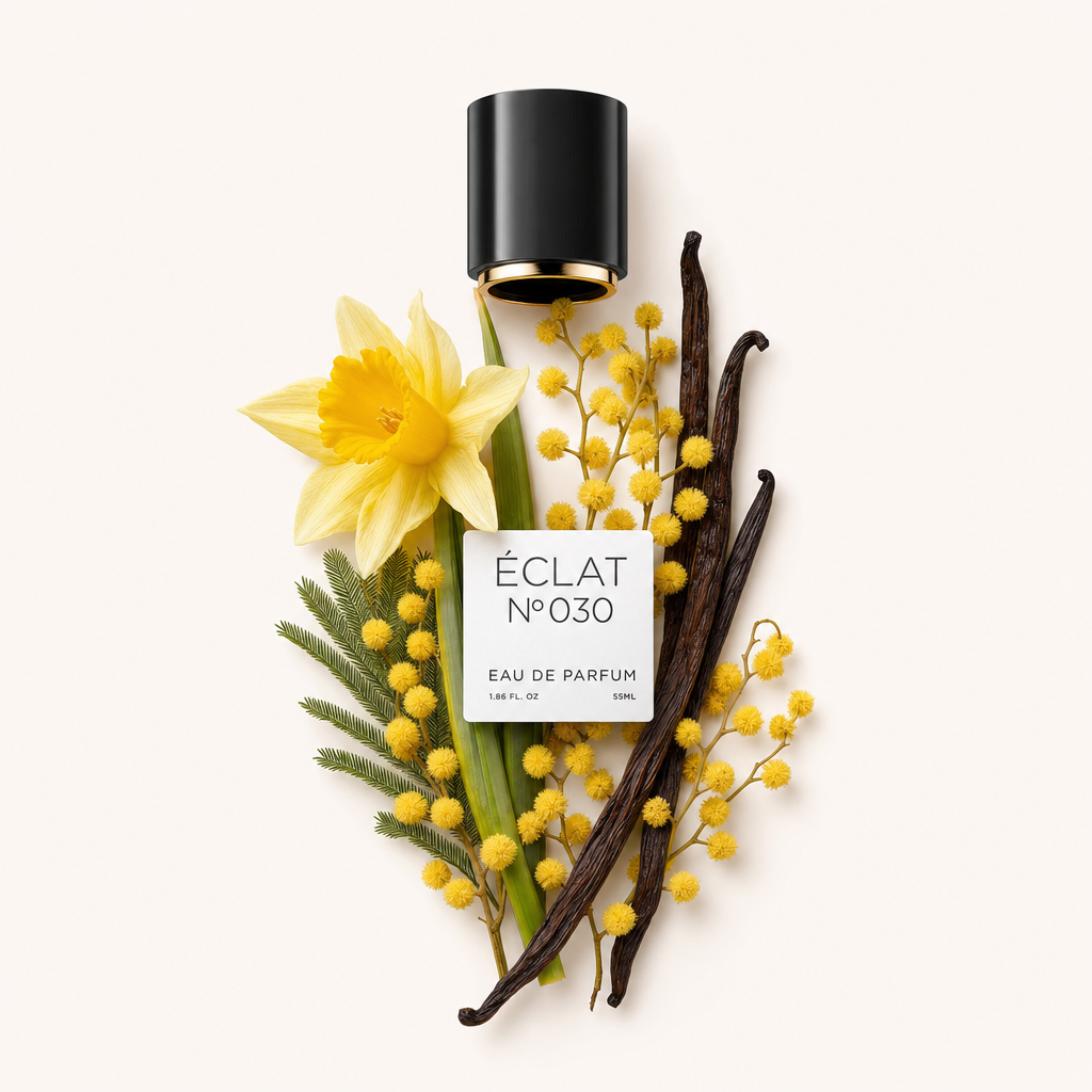 Una composizione di un narciso giallo, rami di mimosa e baccelli di vaniglia con un tappo nero con etichetta ÉCLAT Powdery Daffodil.