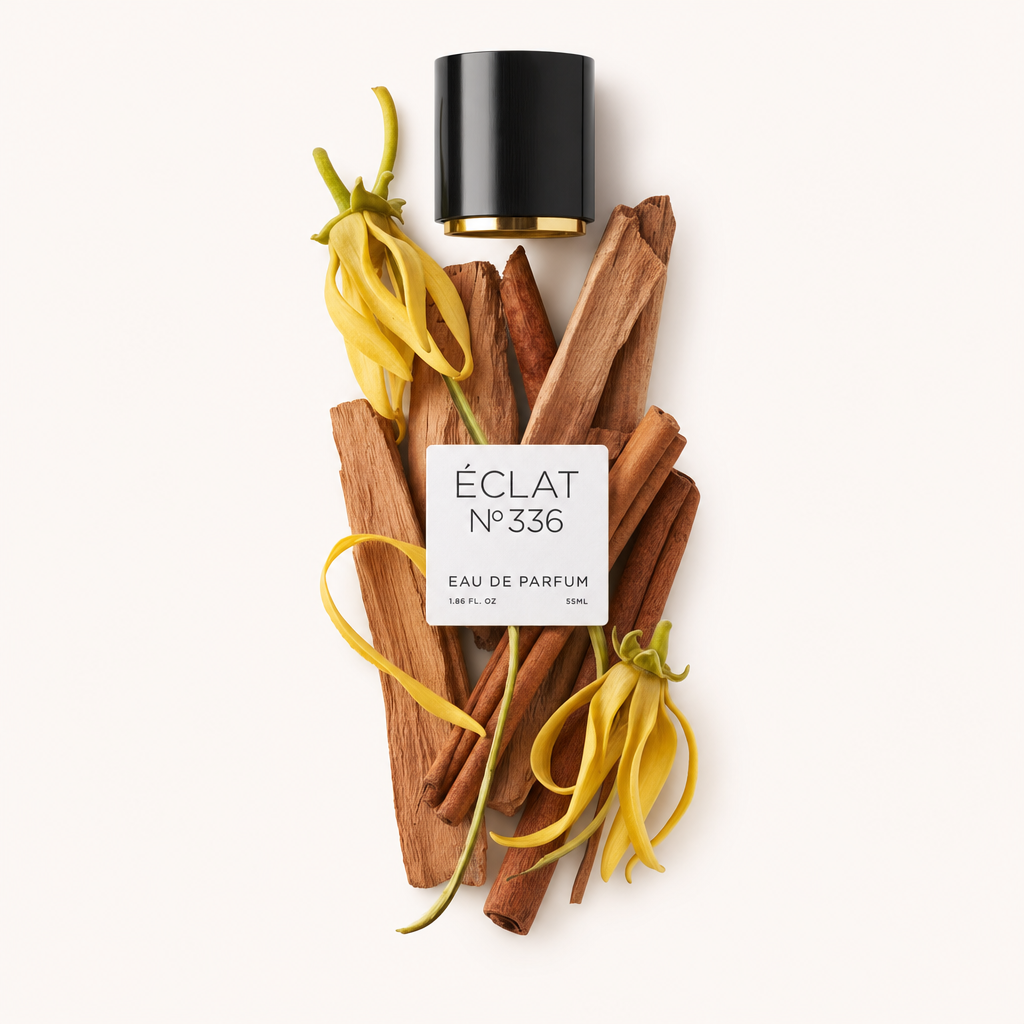 Una composizione di fiori di ylang-ylang gialli e bastoncini di sandalo accompagna un tappo nero con etichetta per ÉCLAT Powdery Sandalwood.