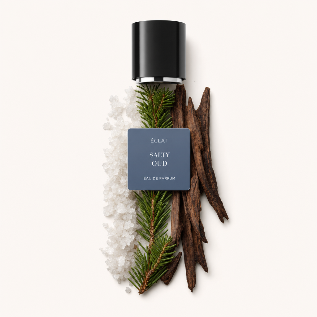 Un arrangiamento di cristalli di sale grosso, ramoscelli di sempreverde e pezzi di legno scuro accanto a un tappo nero con etichetta ÉCLAT Salty Oud.