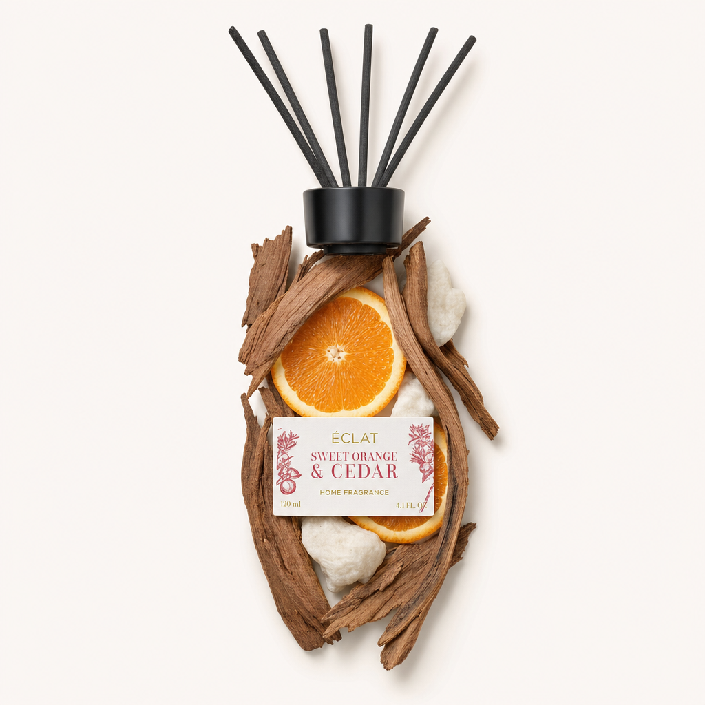 Un arrangiamento di pezzi di legno di cedro e fette di arancia dolce circonda un tappo nero con l'etichetta di ÉCLAT Sweet Orange & Cedar Room Fragrance Sticks.