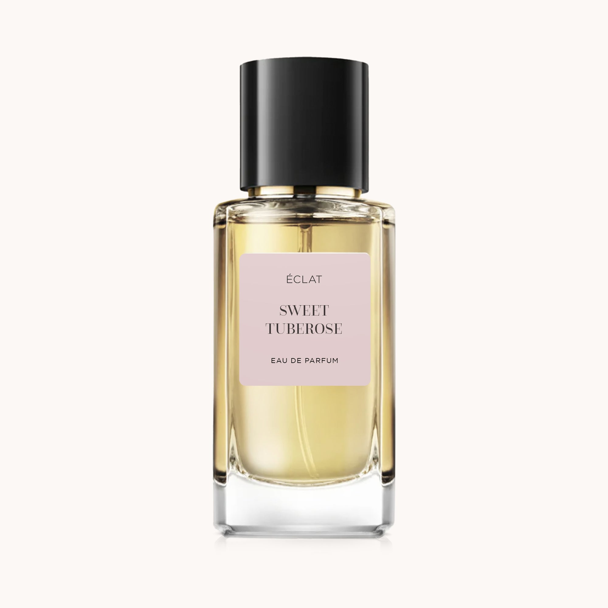 Il profumo ÉCLAT Sweet Tuberose in un flacone di vetro sfaccettato con tappo nero e etichetta rosa pallido.