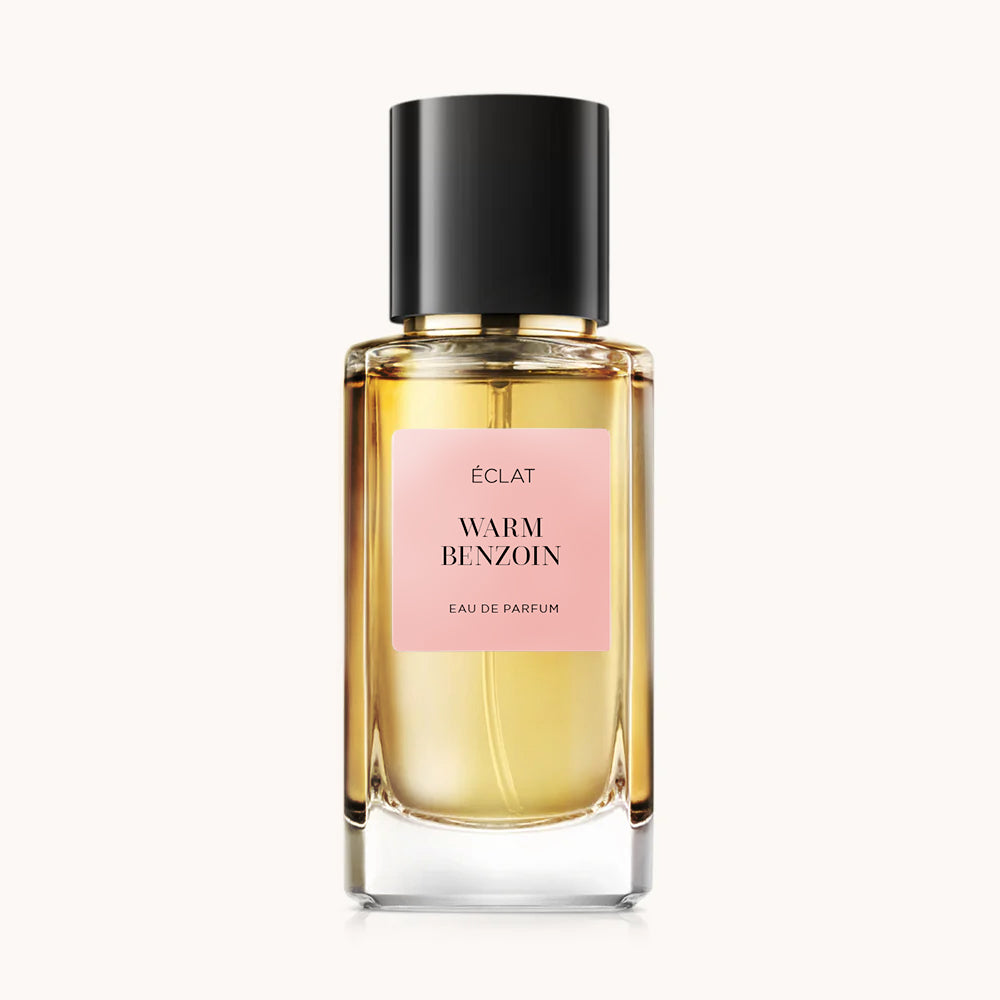 Flacone in vetro sfaccettato di ÉCLAT Warm Benzoin con tappo nero ed etichetta rosa.