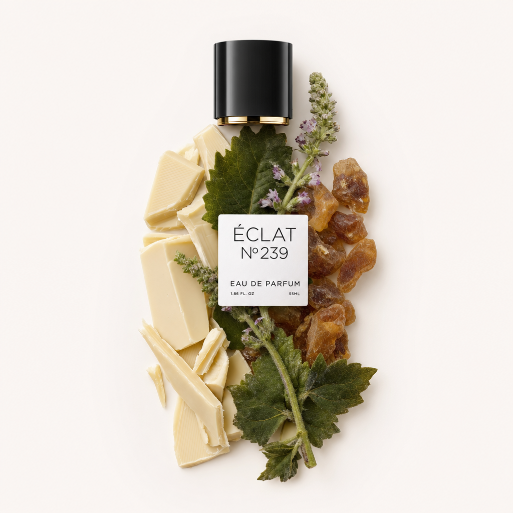 Un arrangiamento di pezzi di cioccolato bianco, foglie fresche di patchouli e resina, con un tappo nero con etichetta ÉCLAT 239.